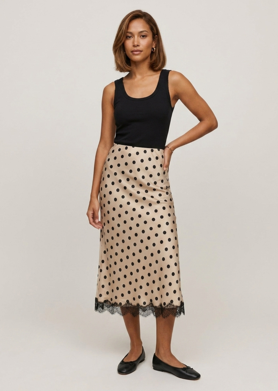 Infused with vintage charm and delicate boudoir-inspired details, this silky slip skirt offers a timeless, romantic feel with an effortless modern edge. Cut in a classic bias-style slip silhouette that drapes softly along the body. It features a mid-rise fit and a graceful midi length hitting just below the knee. Crafted from a silky, champagne-beige satin fabric adorned with contrast black polka dots throughout. The hemline is finished with an intricate, eyelash-trimmed black lace border for an ethereal, l