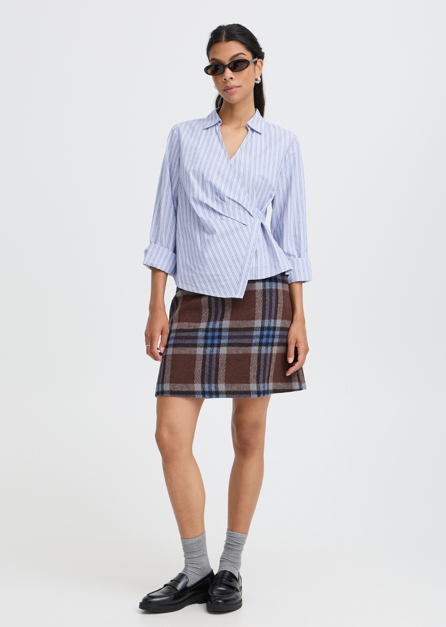 Reimagine classic shirting with this modern wrap blouse. Crafted in light blue with sophisticated vertical stripes, it features a wrap design that secures along the waist, highlighting your natural shape with dynamic crossover pleating and an asymmetrical hemline. The crisp collar and deep V-neck keep it clean and refined, making it the perfect statement piece put with trousers or pair with seasonal skirts.