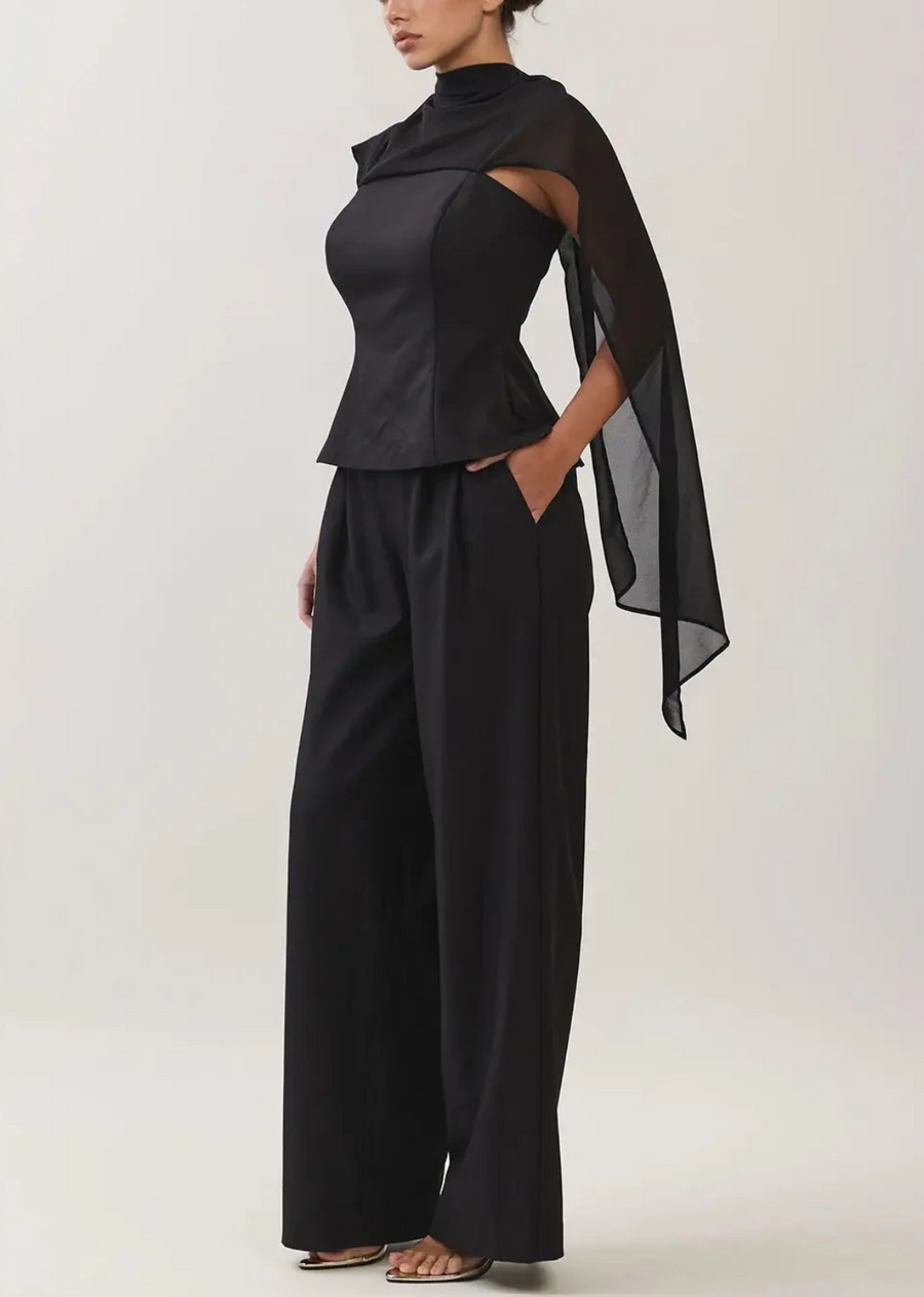 Make a striking statement in the&nbsp;set, a masterclass in modern sophistication. Designed for the fashion-forward wardrobe, this all-black two-piece ensemble pairs a structured, fitted peplum top with fluid, wide-leg trousers for a perfectly balanced silhouette. The standout feature is a sheer, lightweight chiffon overlay that frames the neckline into a chic mock collar and cascades down the back like a dramatic cape. Whether you are dressing for an upscale evening event, a cocktail party, or a stylish di