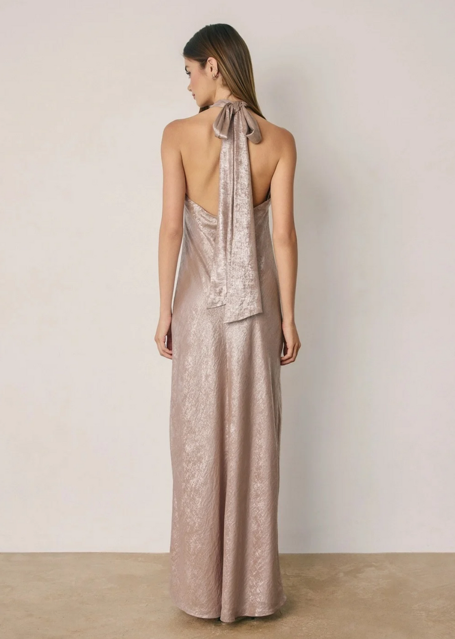 This shimmering halter maxi dress features a sleek, body-skimming silhouette with a statement ring detail at the neckline for a modern, elevated finish.

Crafted from lustrous metallic fabric with a graceful drape, it's the perfect choice for weddings, formal events, and evening occasions. The Editorial model is 5'9" and E-comm model is 5'9". They are wearing size Small.