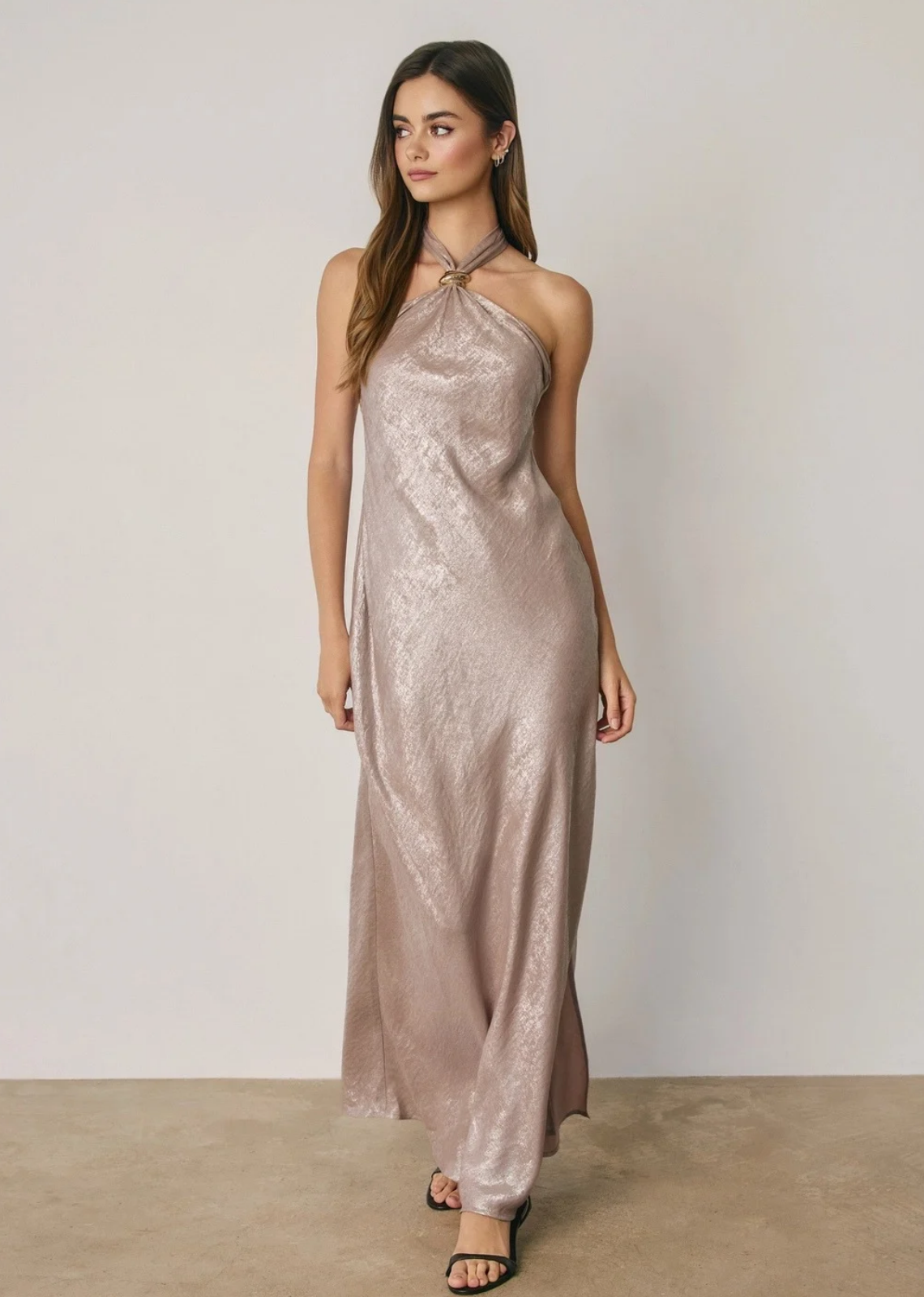 This shimmering halter maxi dress features a sleek, body-skimming silhouette with a statement ring detail at the neckline for a modern, elevated finish.

Crafted from lustrous metallic fabric with a graceful drape, it's the perfect choice for weddings, formal events, and evening occasions. The Editorial model is 5'9" and E-comm model is 5'9". They are wearing size Small.