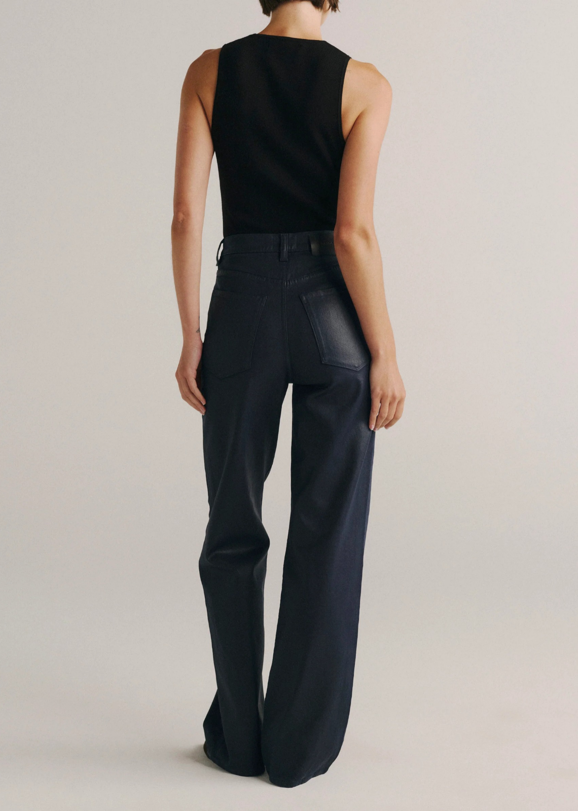 Karmine high-rise wide-leg jeans in deep navy blue coated denim with a leather-like finish, silver hardware, tonal stitching, a clean hem, and a black back patch. Designed with a flattering sculpted fit and a 32-inch inseam.