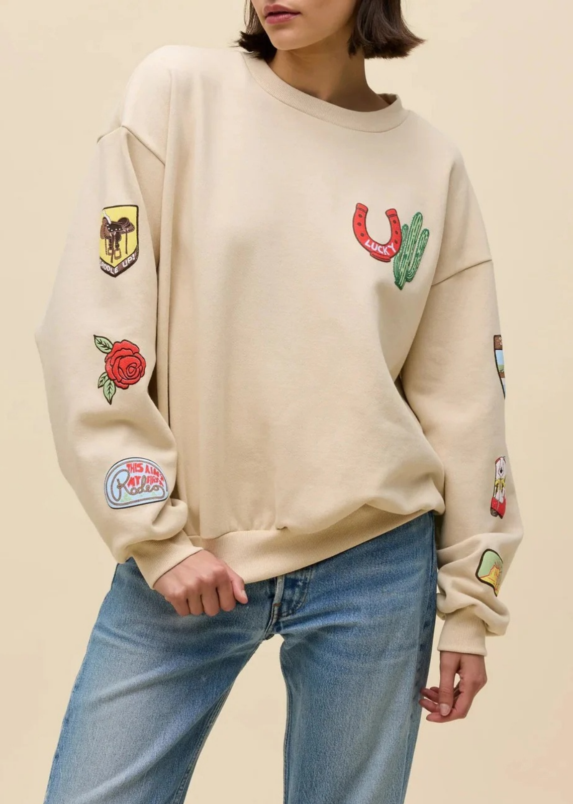Add a touch of western charm to your casual wardrobe with this vintage-inspired graphic sweatshirt. Cut in a relaxed, relaxed-fit silhouette with dropped shoulders and classic ribbed trims, this cozy pullover features vibrant embroidered patches throughout. From a lucky horseshoe and Saguaro cactus on the chest to colorful cowboy boots, and western badges down the sleeves, every detail brings playful personality to an effortless off-duty look.
