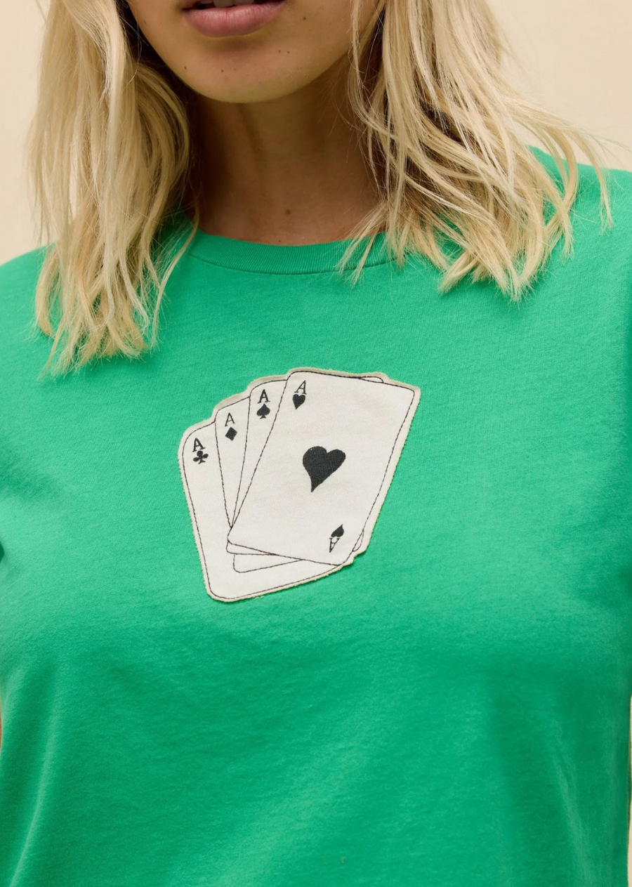 Deal yourself a winning look with this vibrant graphic tee. Crafted in a bold lucky green hue, this classic crewneck features a subtle, vintage-inspired front graphic showcasing a hand of four Ace playing cards. Cut in a relaxed yet classic fit, it’s designed to bring a touch of playful charm to your everyday wardrobe. Pair it with tailored black trousers for a sleek high-low contrast or throw it on with your favorite vintage denim for an effortless weekend vibe.