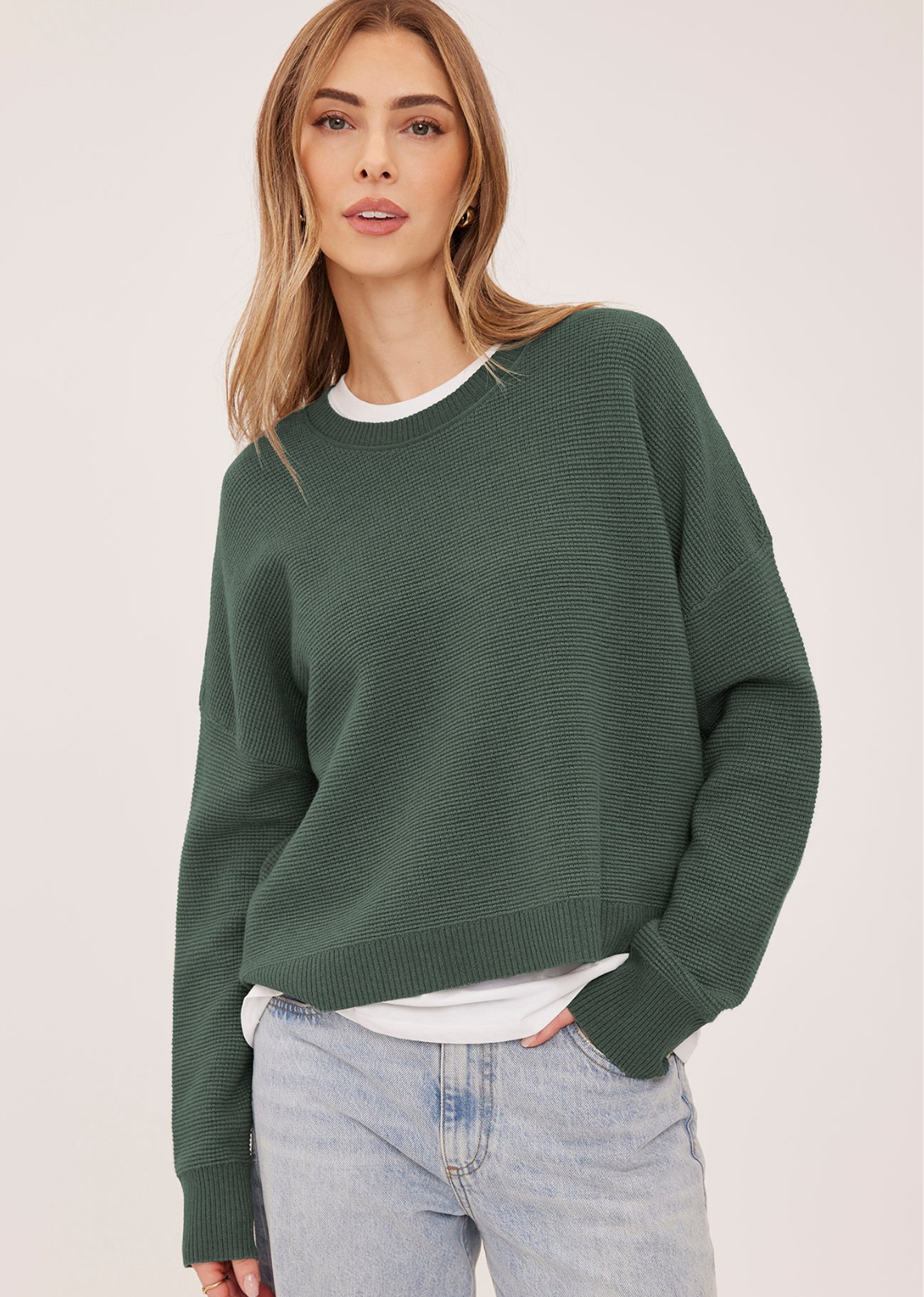 The Axel sweater is made of a soft yarn in a waffle knit pattern. Features include a crew neckline, exposed seam details, and side slits.