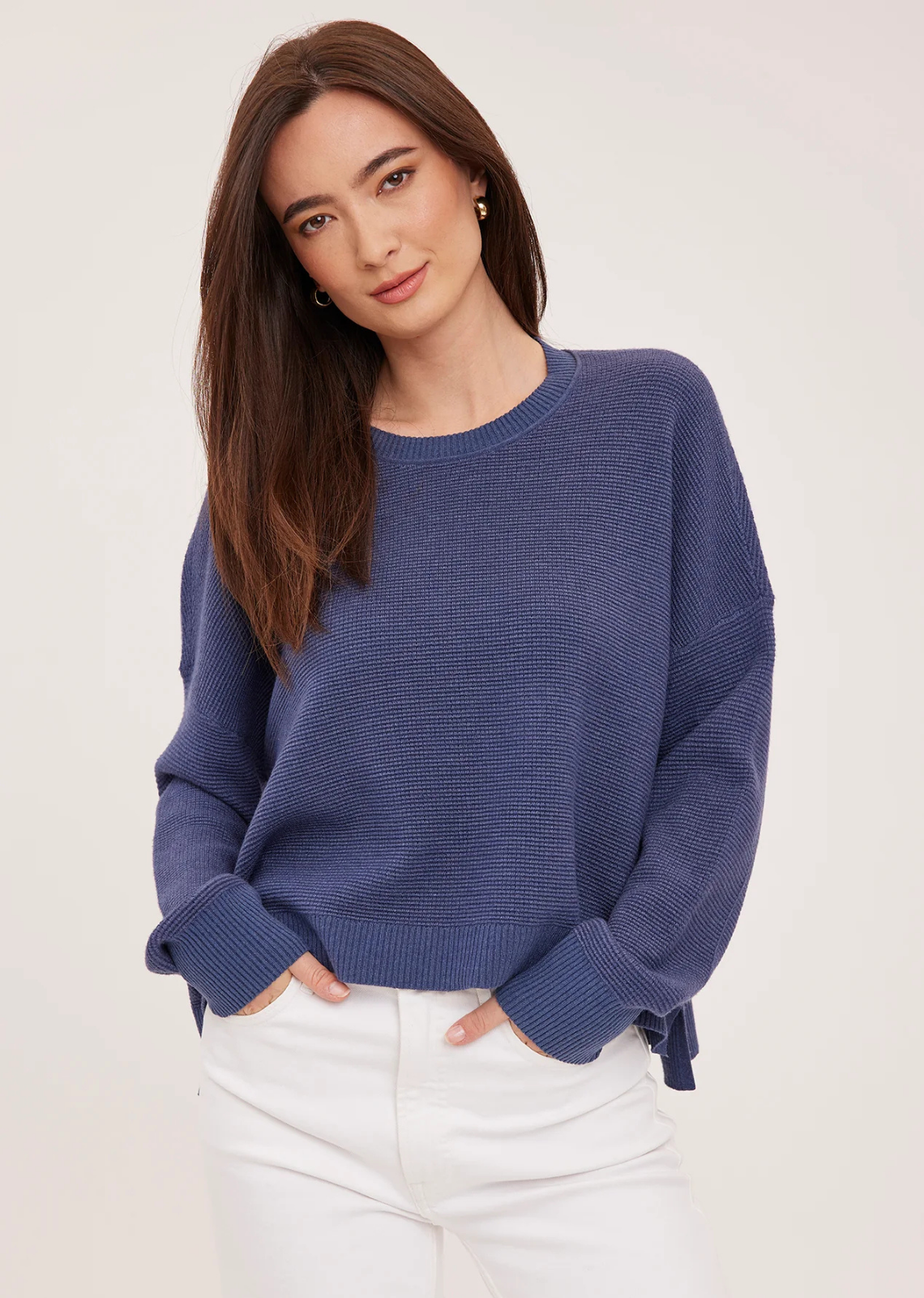 The Axel sweater is made of a soft yarn in a waffle knit pattern. Features include a crew neckline, exposed seam details, and side slits.
