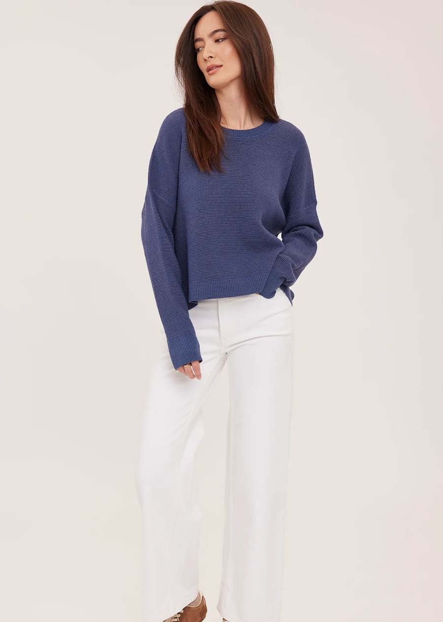 The Axel sweater is made of a soft yarn in a waffle knit pattern. Features include a crew neckline, exposed seam details, and side slits.