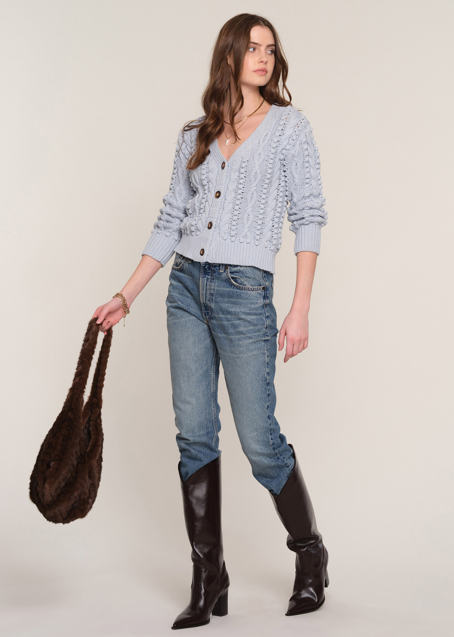 Cozy meets timeless style in this beautifully crafted cable knit cardigan. Designed in a soft, dreamy light blue hue, this sweater features an intricate cable knit pattern with charming bobble detailing for added texture and dimension. The flattering V-neckline and oversized tortoise-style buttons create a classic look, while the ribbed cuffs and hem provide a comfortable, polished fit.