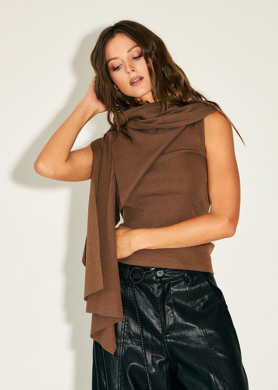 Elevate your transitional wardrobe with this cape overlay knit top. Designed with a chic layered construction, this piece features a fitted, sleeveless base paired with a dramatic, flowing caped overlay that drapes over the shoulders and arms for a striking silhouette. The soft, warm neutral tone makes it an exceptionally versatile piece to pair with everything from sleek faux-leather trousers to tailored skirts.