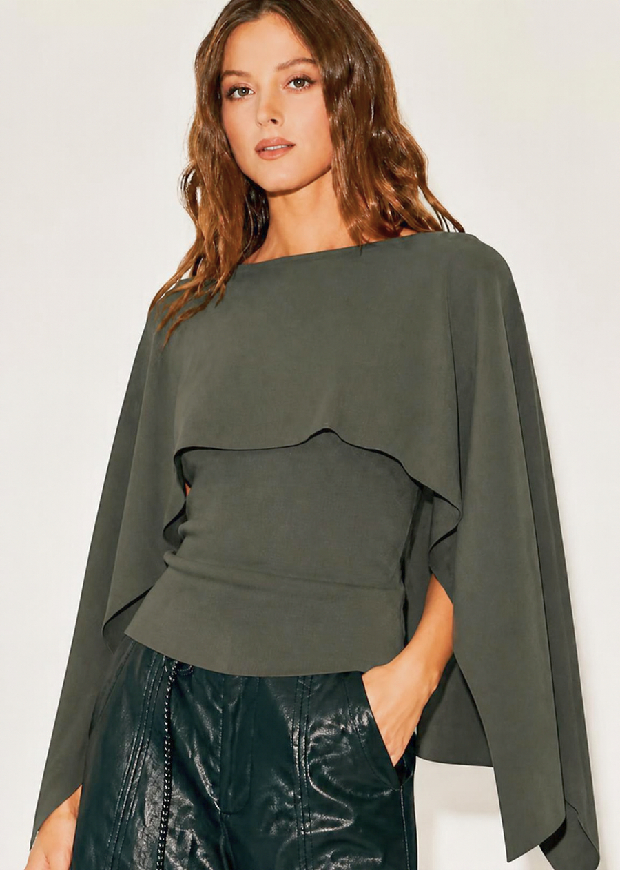Elevate your transitional wardrobe with this cape overlay knit top. Designed with a chic layered construction, this piece features a fitted, sleeveless base paired with a dramatic, flowing caped overlay that drapes over the shoulders and arms for a striking silhouette. The soft, warm neutral tone makes it an exceptionally versatile piece to pair with everything from sleek faux-leather trousers to tailored skirts.