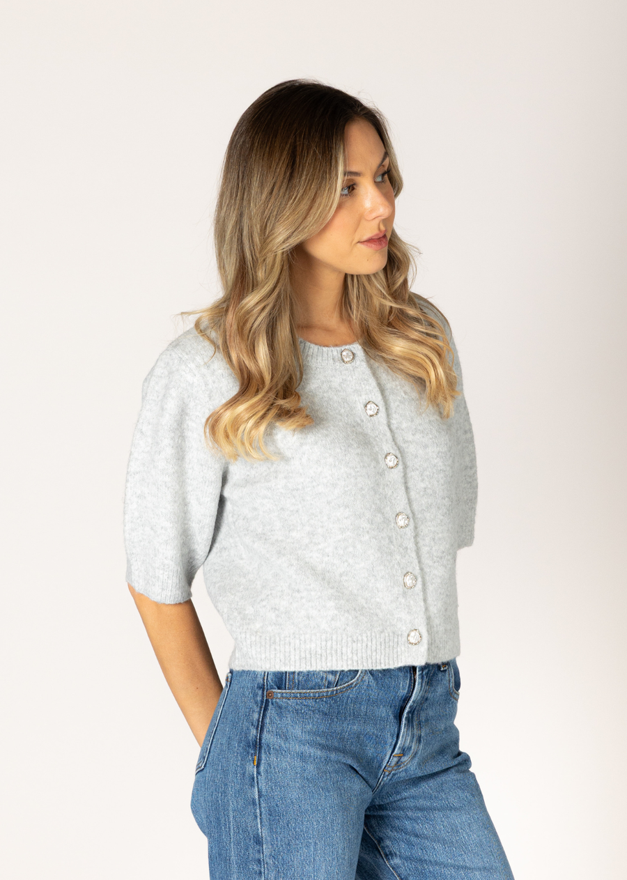 This eco-friendly cardigan is adorned with beautiful irregular pearls set in silver buttons, adding a charming and feminine touch to its classic design. Perfect for layering, it combines style and elegance with a unique button detail for a refined look.