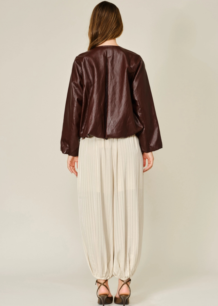 A modern take on the classic bomber, the Merlot Jacket is crafted from soft vegan leather in a rich mahogany hue. Designed with a clean round neckline, relaxed balloon silhouette, and subtle pleated detailing, it brings effortless structure and elevated edge to any look. Finished with elasticized cuffs and hem, this versatile jacket is made for easy layering throughout the cooler seasons.