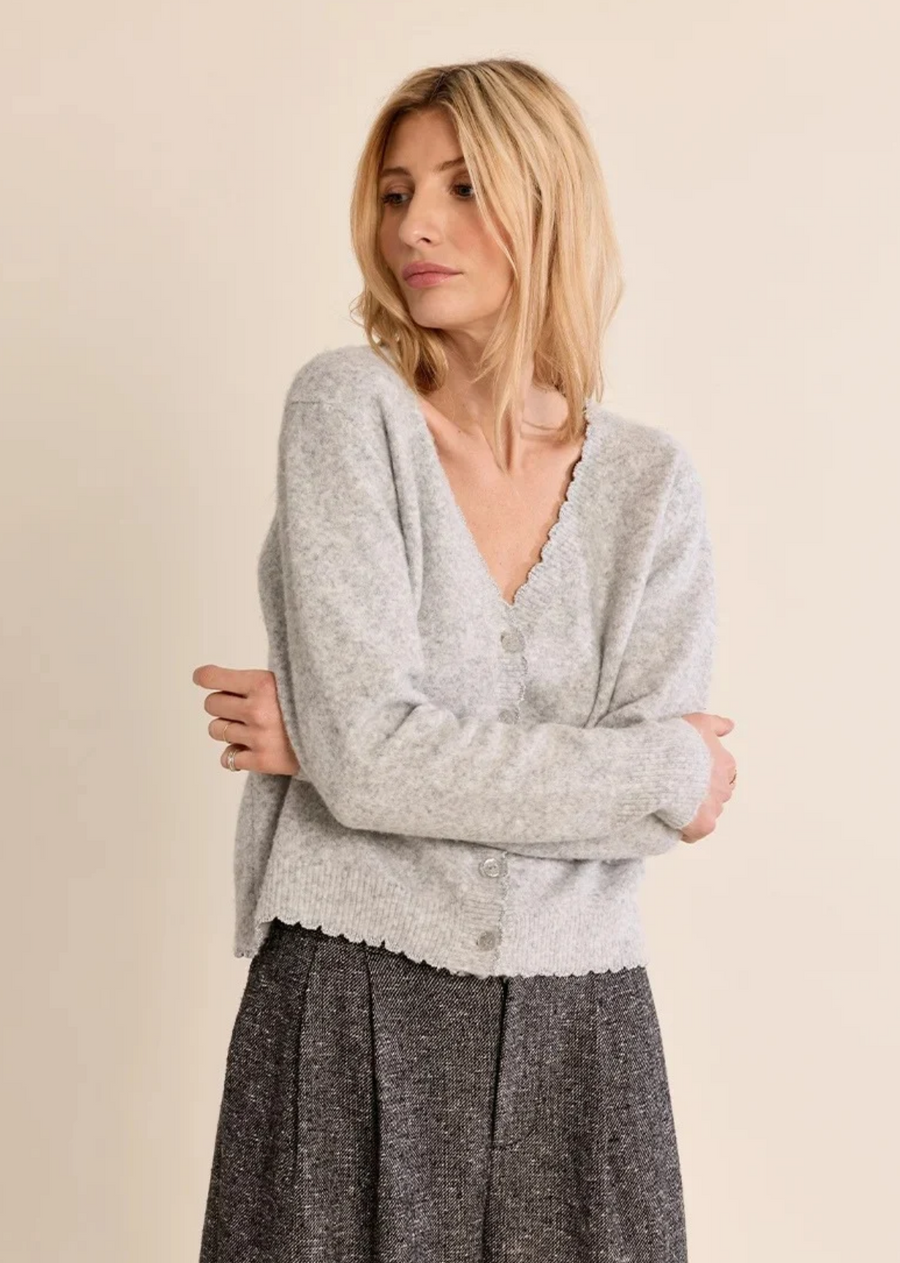 Soft, cozy, and subtly romantic, this heather grey cardigan is an instant wardrobe classic. Crafted from a brushed, plush knit, it features delicate scalloped trim along the flattering V-neckline, button placket, and hemline. Designed with a relaxed fit and button-down front, it bridges the gap between everyday comfort and polished style. Pair it with high-waisted tailored trousers for an elevated office look or slip it on over tailored denim for relaxed weekend layering