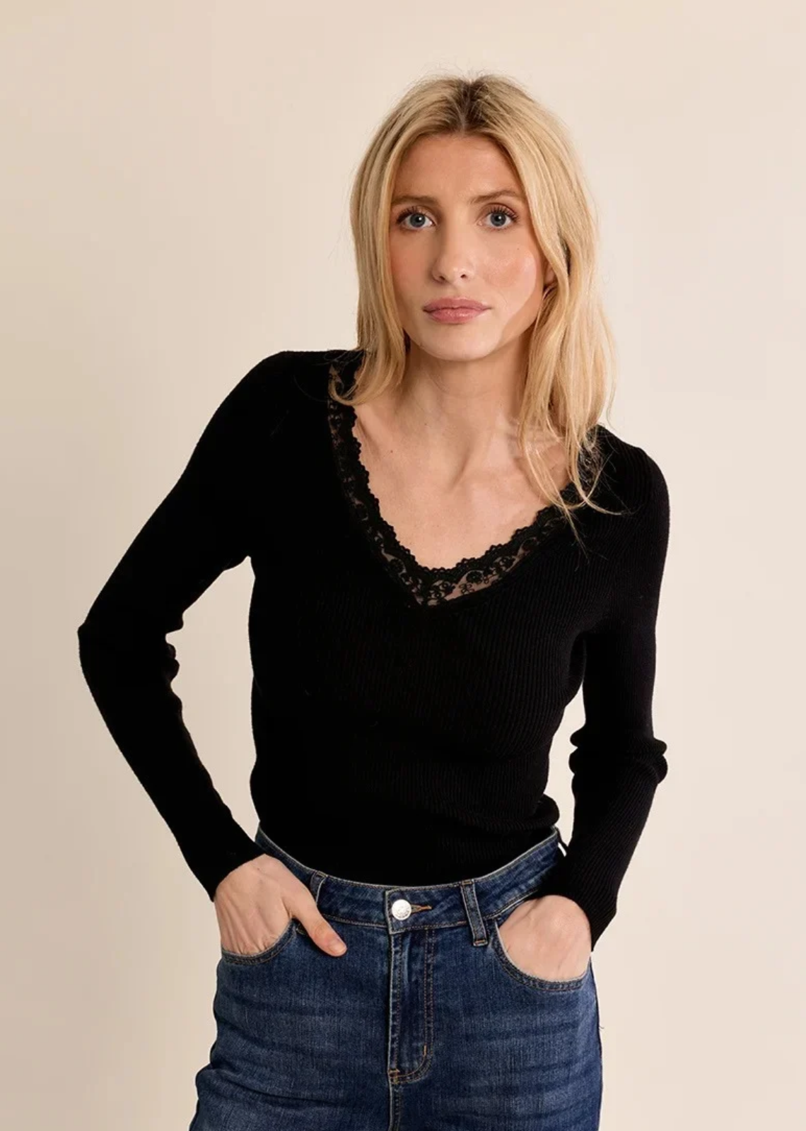 A timeless wardrobe staple with a delicate feminine touch, this long-sleeve knit top is cut from a finely ribbed black fabric that softly hugs the silhouette. It features a flattering V-neckline framed with intricate tonal eyelash lace trim, adding subtle elegance to an everyday favorite.