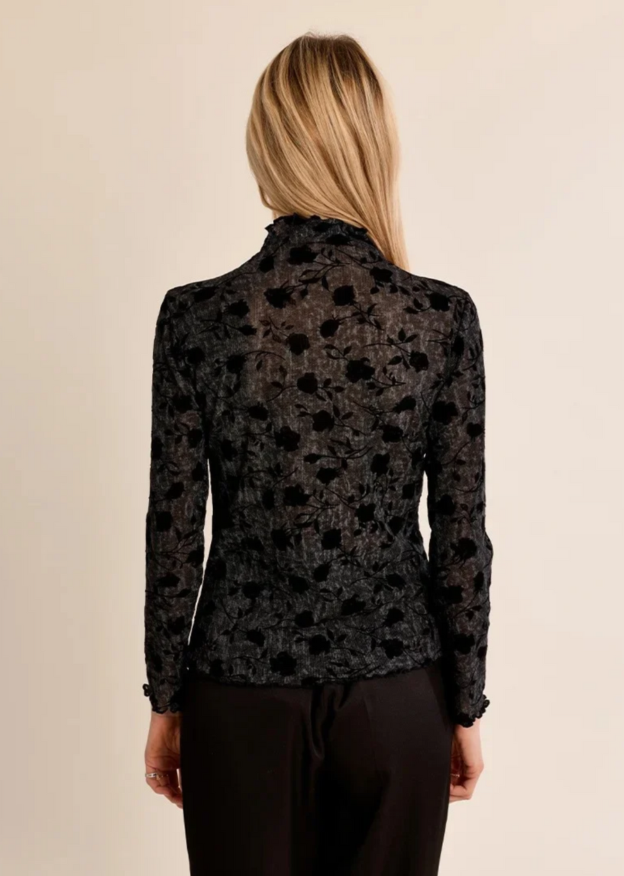Elevate your layering game with this sheer, dark-floral turtleneck top. Crafted from lightweight, subtly textured mesh fabric, this long-sleeve piece features flocked velvet rose motifs throughout, creating a moody, romantic contrast. High-neck detailing and delicately lettuce-hemmed edges at the collar, cuffs, and hem add a refined, subtle finish
