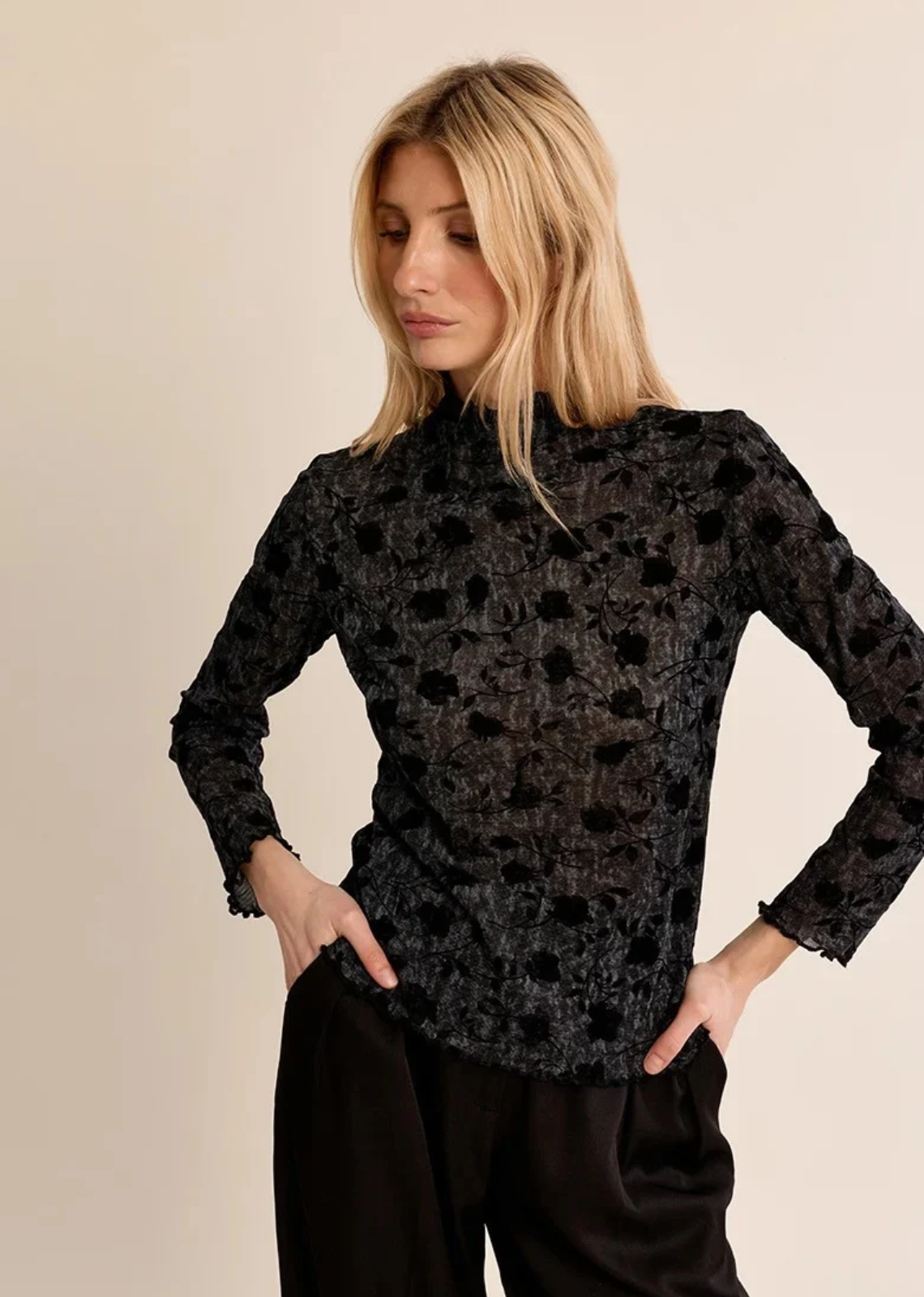 Elevate your layering game with this sheer, dark-floral turtleneck top. Crafted from lightweight, subtly textured mesh fabric, this long-sleeve piece features flocked velvet rose motifs throughout, creating a moody, romantic contrast. High-neck detailing and delicately lettuce-hemmed edges at the collar, cuffs, and hem add a refined, subtle finish