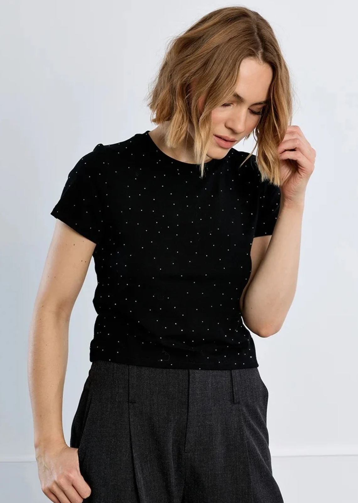 Elevate your everyday tee rotation with this chic, studded classic. Crafted from soft black cotton knit, this fitted short-sleeve tee is dusted with delicate, micro-rhinestone pinpoints that catch the light with every move. Designed with a timeless crew neck and a clean, straight hemline, it offers the perfect balance of effortless edge and playful sparkle. Tuck it into high-waisted tailored trousers for a night out, or pair it with relaxed denim and a leather jacket for casual street-style glamour.