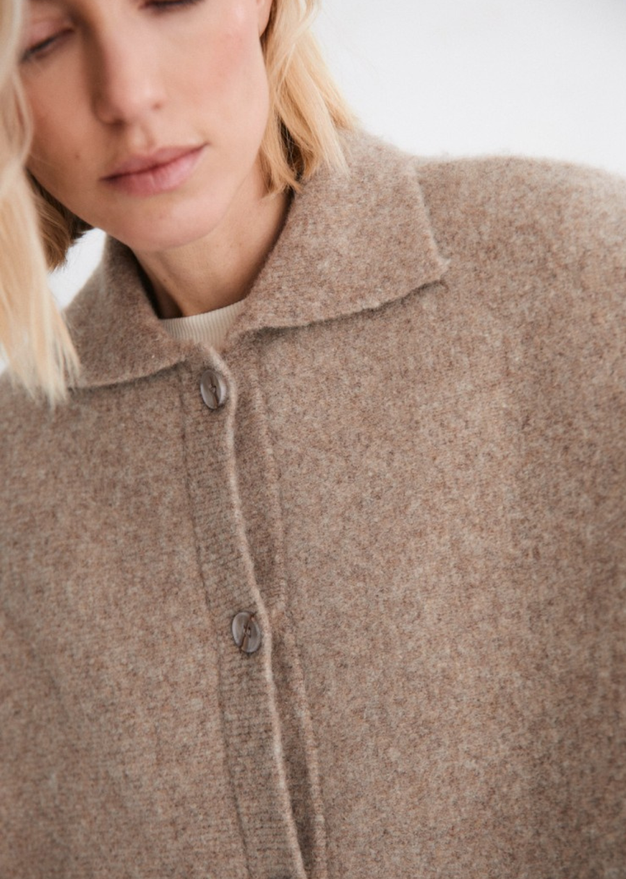 Knitted cape with a shirt collar, front button placket and ribbed finishes, offering functionality and understated sophistication.