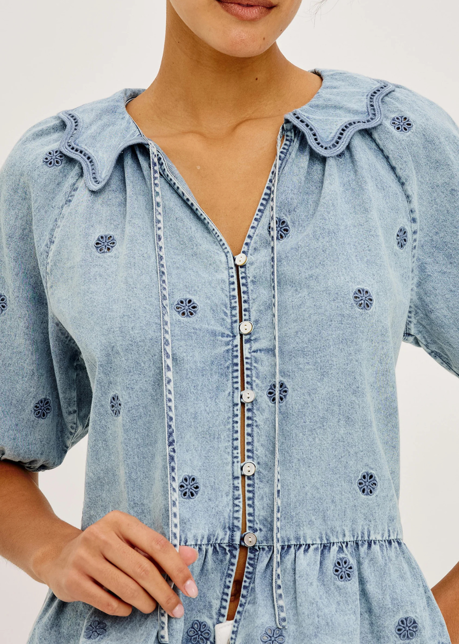 The Emelie is a drapey denim shirt with a self-tie V-neckline, front buttons, and a relaxed fit. Finished with an embroidered collar, short puff sleeves, and a peplum hem for an effortlessly feminine look.