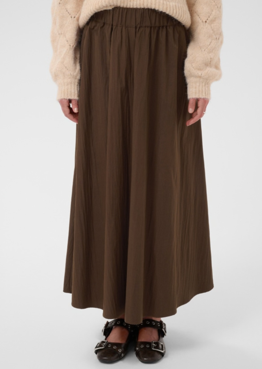 This long skirt features a wide, gently flared silhouette with an elasticated waistband for a comfortable fit. The material has a slightly crinkled appearance, offering a soft, flowing drape. There are no visible embellishments or additional details.
