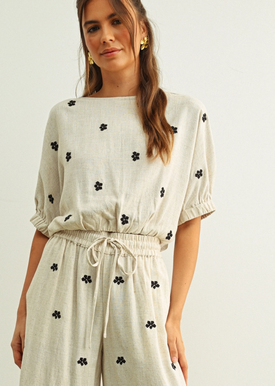 An effortlessly feminine top designed with a relaxed silhouette and soft gathered details. Featuring delicate puff sleeves, a breezy boat neckline, and subtle black floral embroidery scattered throughout, this lightweight neutral piece brings an easy elegance to everyday dressing. Pair it with the matching pant or your favourite denim for a polished yet laid-back look.