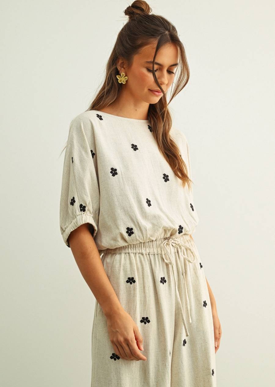 An effortlessly feminine top designed with a relaxed silhouette and soft gathered details. Featuring delicate puff sleeves, a breezy boat neckline, and subtle black floral embroidery scattered throughout, this lightweight neutral piece brings an easy elegance to everyday dressing. Pair it with the matching pant or your favourite denim for a polished yet laid-back look.