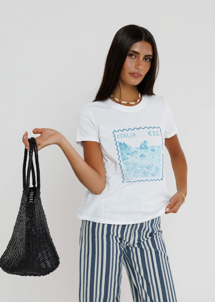 Capture the charm of the Italian coast with this effortlessly chic graphic tee. Featuring a vintage-inspired "Italia" postage stamp graphic in soft coastal blue hues, this tee brings a timeless, travel-inspired feel to your everyday wardrobe. Designed with a classic crew neckline and an easy, relaxed fit, it's the perfect piece to pair with striped linen pants, denim, or shorts for an effortlessly polished summer look.