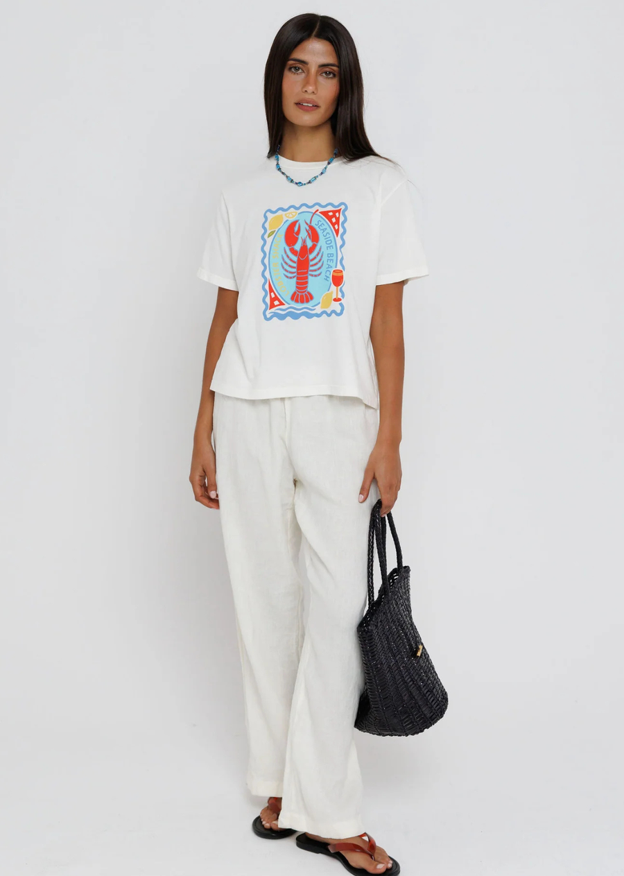 Bring a splash of coastal charm to your everyday wardrobe with this playful graphic tee. Featuring a vibrant lobster illustration framed by seaside-inspired details in bold shades of blue, red, and yellow, this relaxed tee captures the carefree spirit of summer. Finished with a classic crew neckline and an easy fit, it's the perfect piece to pair with linen pants, denim, or your favorite shorts for effortless warm-weather style.