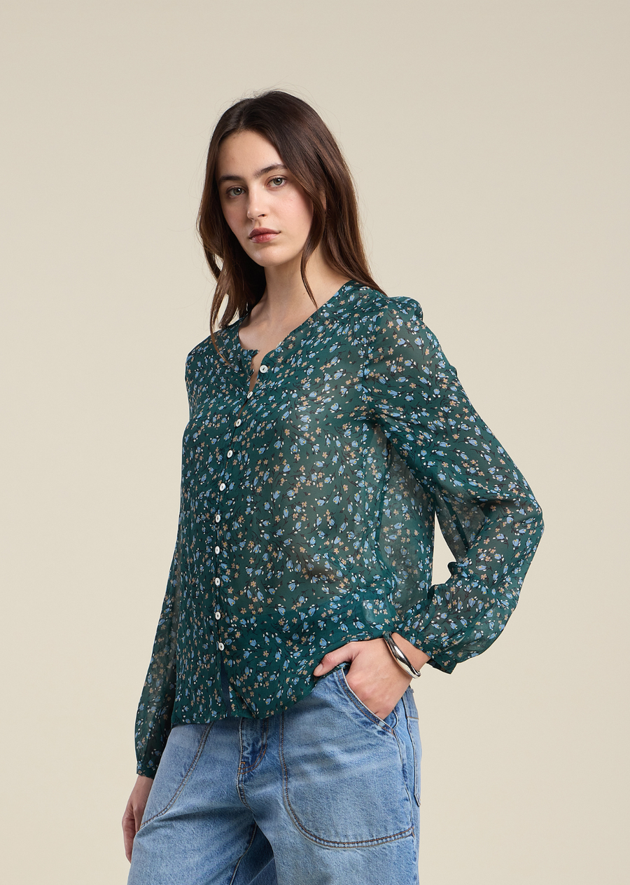 This look exudes a relaxed, bohemian vibe, perfect for a casual day out. The central piece is a sheer, lightweight blouse in a rich, dark teal-green hue. It features a charming all-over micro-floral print with delicate touches of light blue and rust-orange flowers. The blouse is designed with a high, collarless neck and a full button-down front, punctuated by small, contrasting white buttons. Its loose, airy fit is enhanced by slightly billowy, long sleeves that finish with subtly gathered cuffs.