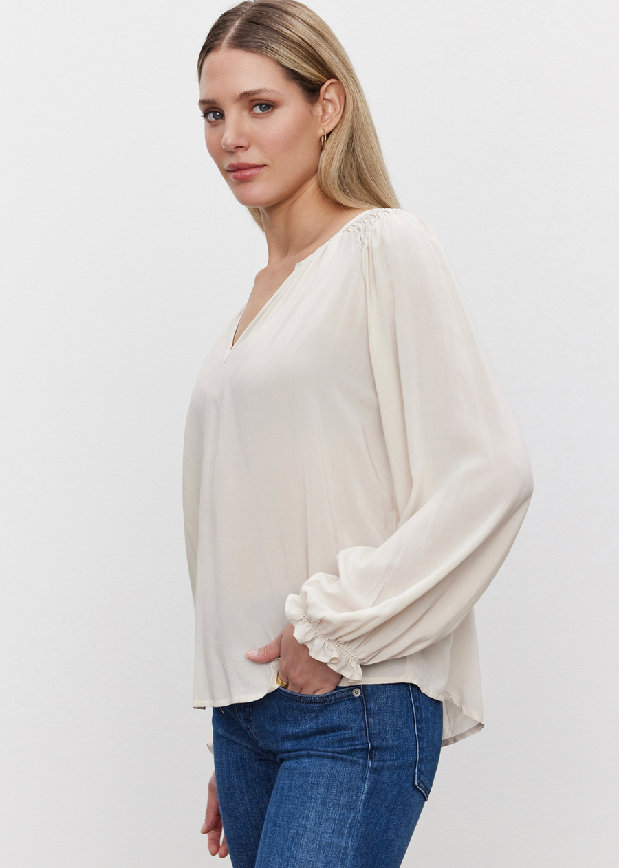 Velvet Azalea Blouse.The Azalea Blouse is crafted from rayon challis for a soft and lightweight feel. It includes a v-neckline, smocked shoulder detail, elastic ruffle cuffs, and a scooped hemline. Its slight sheen and draped fit make it a versatile choice for any wardrobe.