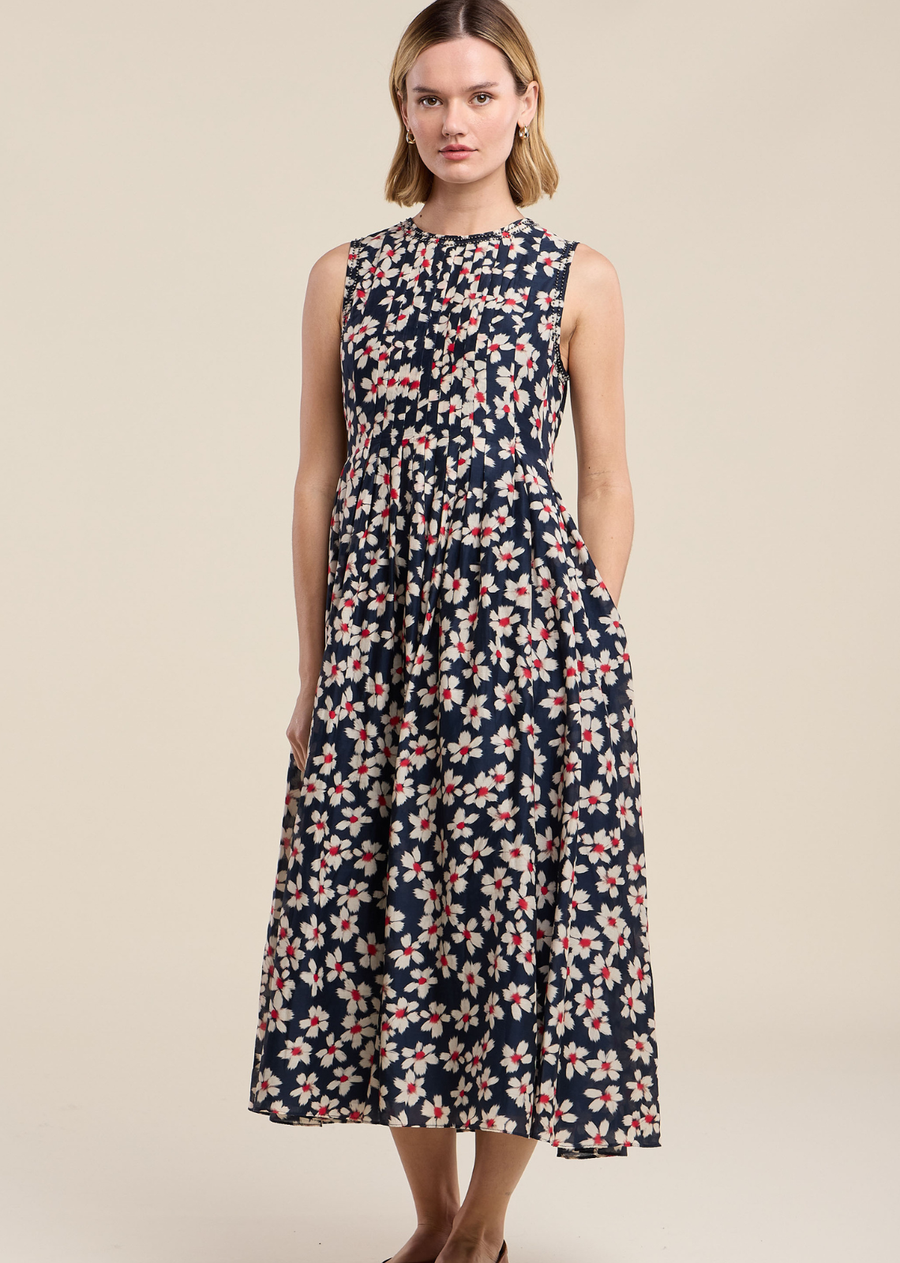 This graceful sleeveless midi dress features an all-over autumn bloom print, showcasing cream and crimson red floral motifs set against a rich navy backdrop. Designed with a fitted bodice, it highlighted delicate pintuck pleating across the chest and subtle lace trim framing the high neckline and armholes. The skirt gathers softly at the waist, falling into a flared, floaty A-line silhouette with convenient side pockets that hit near the ankle.