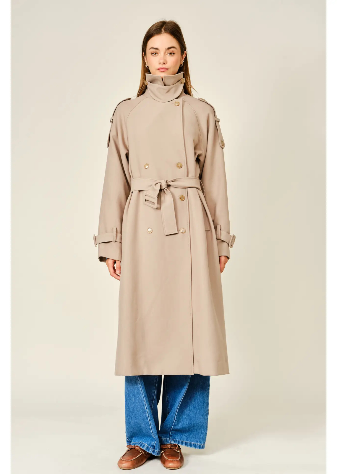 Tan longline trench coat with a relaxed fit, layered neckline, double-button closure, and adjustable waist belt.
