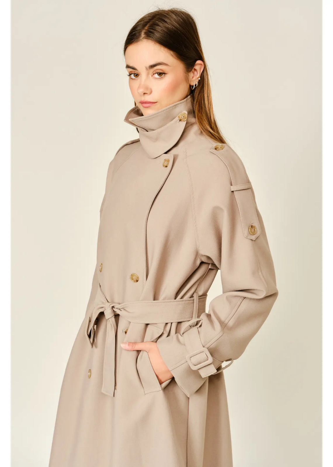 Tan longline trench coat with a relaxed fit, layered neckline, double-button closure, and adjustable waist belt.