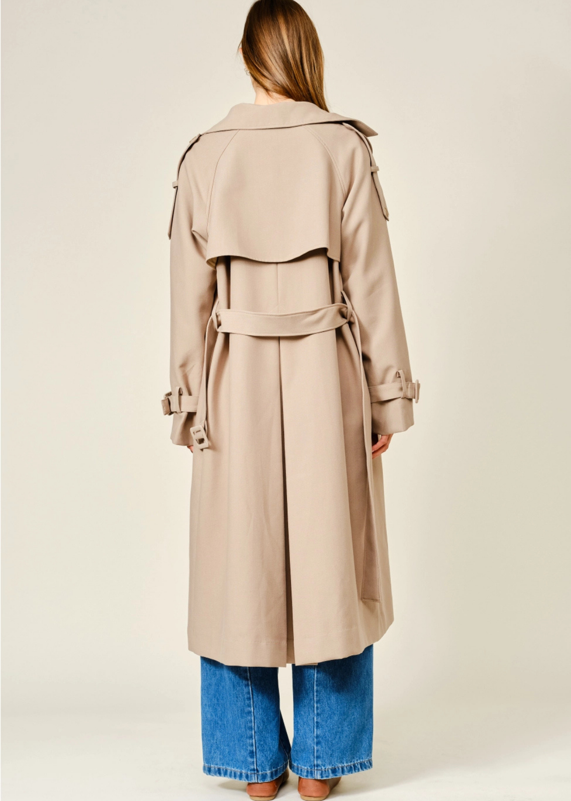 Tan longline trench coat with a relaxed fit, layered neckline, double-button closure, and adjustable waist belt.