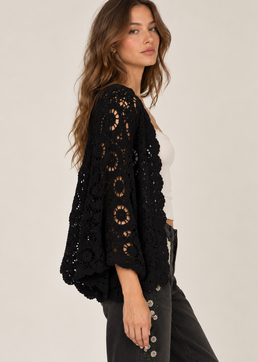 Model wearing the Journi black crochet cardigan with floral detailing and scalloped edges over a white tank top and black jeans.