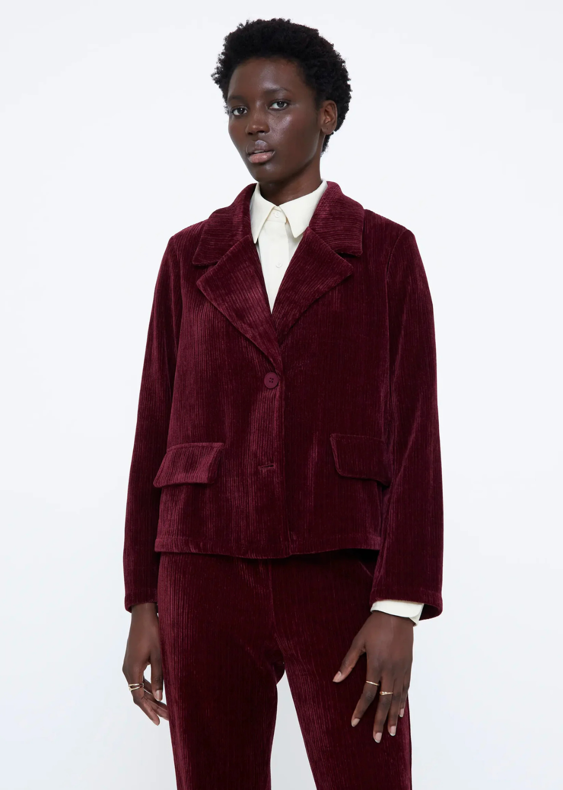 Burgundy velvet blazer with a lapel collar, long sleeves, front button closure, front pockets, and inner lining.